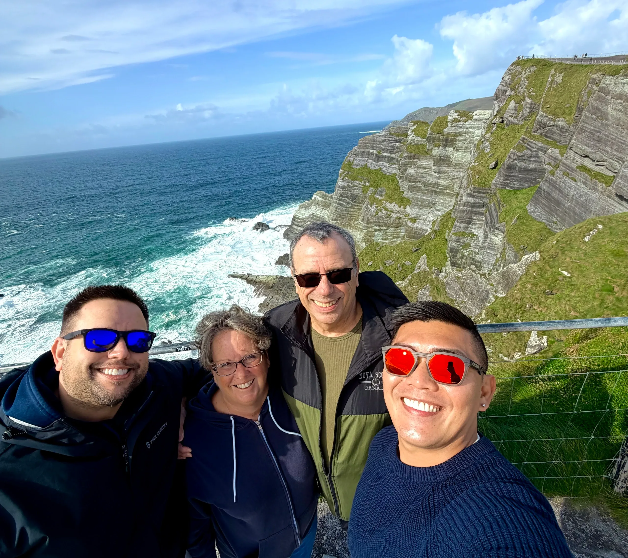 Four family members smiling at the Kerry Cliffs, with layered rock faces and Atlantic waves behind them.